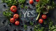 Tomatoes, herbs, olives, celery and a YES sign in the centre. Say yes to vitamin vegetables! Chalk on a black board saying YES. Talk to vegetables more often, they are great conversationalists