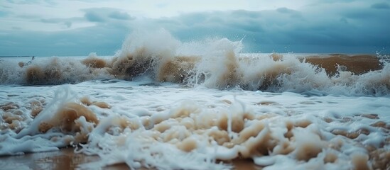 Poster - A large and forceful wave crashes onto the sandy shore of a beach, creating a dramatic display of water and foam. The waves energy sends water spraying into the air, while the force of the impact