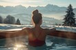 a young beautiful woman on ski vacation relaxing with her back turned in a warm soapy bathtub looking at the snowy mountains enjoying the view
