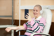 © Seventyfour - Portrait of smiling bald woman receiving IV treatment in clinic and talking via video chat copy space