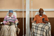 © Seventyfour - Front view at two people sitting in chairs with IV drip tubes and getting chemotherapy treatment in clinic