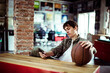 © Davor - Young man with basketball sitting and using smartphone in startup office
