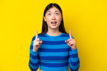 Wall Mural - Young Chinese woman isolated on yellow background surprised and pointing up