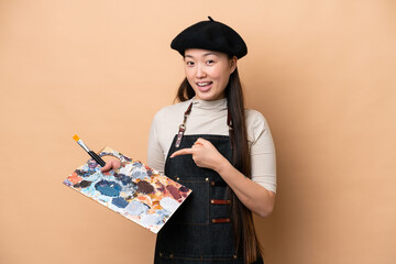 Wall Mural - Young Chinese painter woman isolated on beige background pointing to the side to present a product