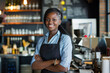 confident African American woman smiling, wearing a denim shirt and black apron, standing in a coffee shop.