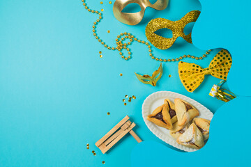 Wall Mural - Purim holiday concept with carnival mask, noisemaker and hamantaschen cookies on blue background. Top view, flat lay composition