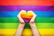 Female hands holding heart on rainbow flag background. LGBT pride concept. LGBT Concept with Copy Space. Pride Month Concept.