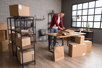 Wall Mural - Male online store seller with shoes talking by mobile phone at table in warehouse