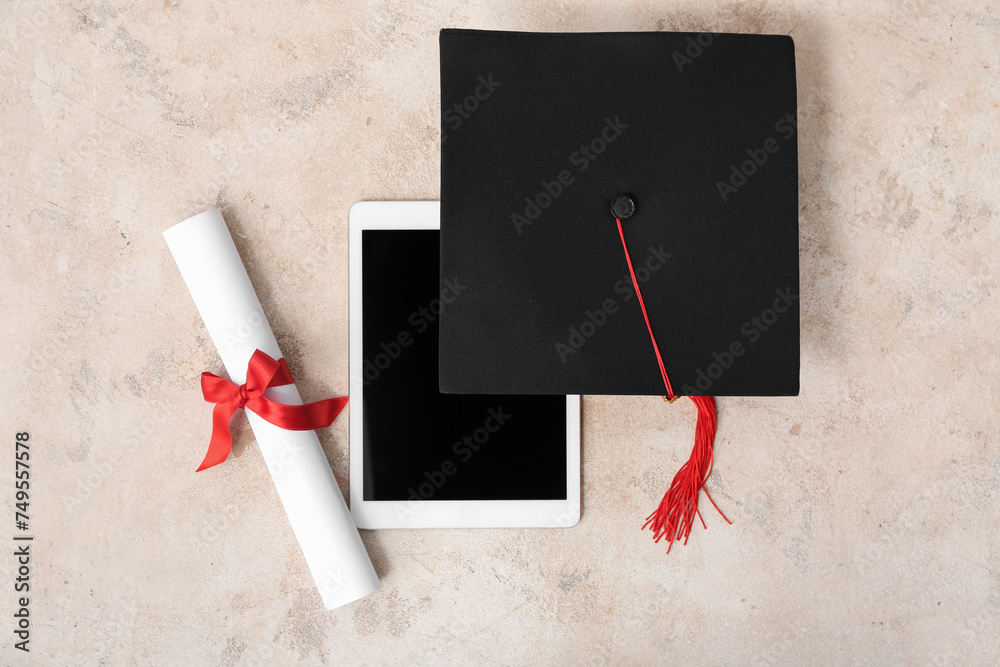 Mortar board with diploma and modern tablet computer on beige background
