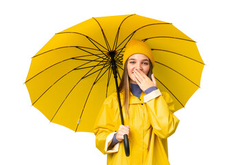 Canvas Print - Teenager girl with rainproof coat and umbrella over isolated chroma key background happy and smiling covering mouth with hand