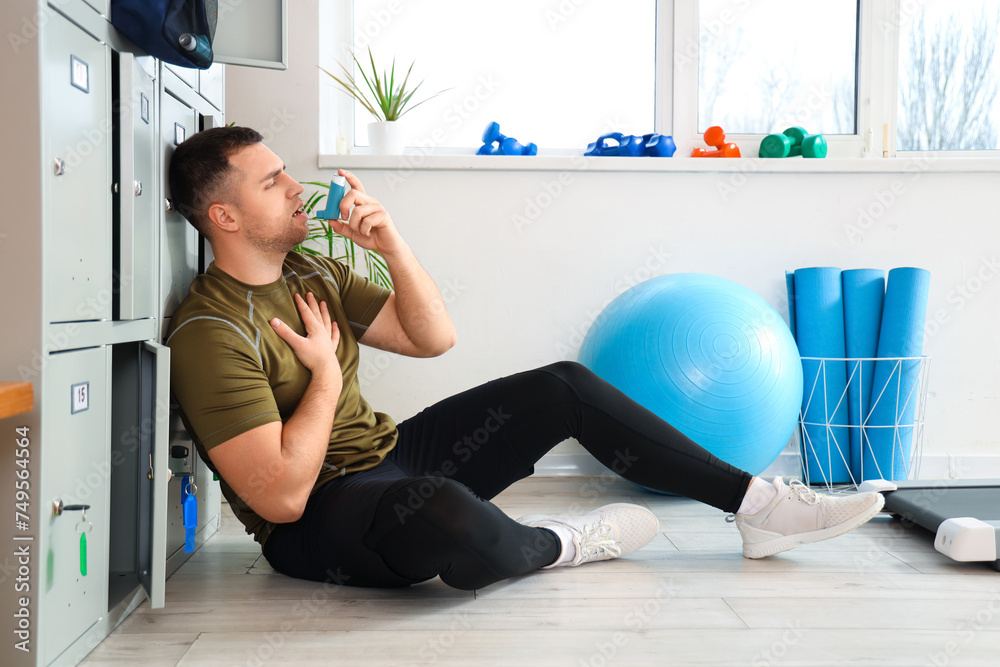 Sporty young man using inhaler near locker in gym