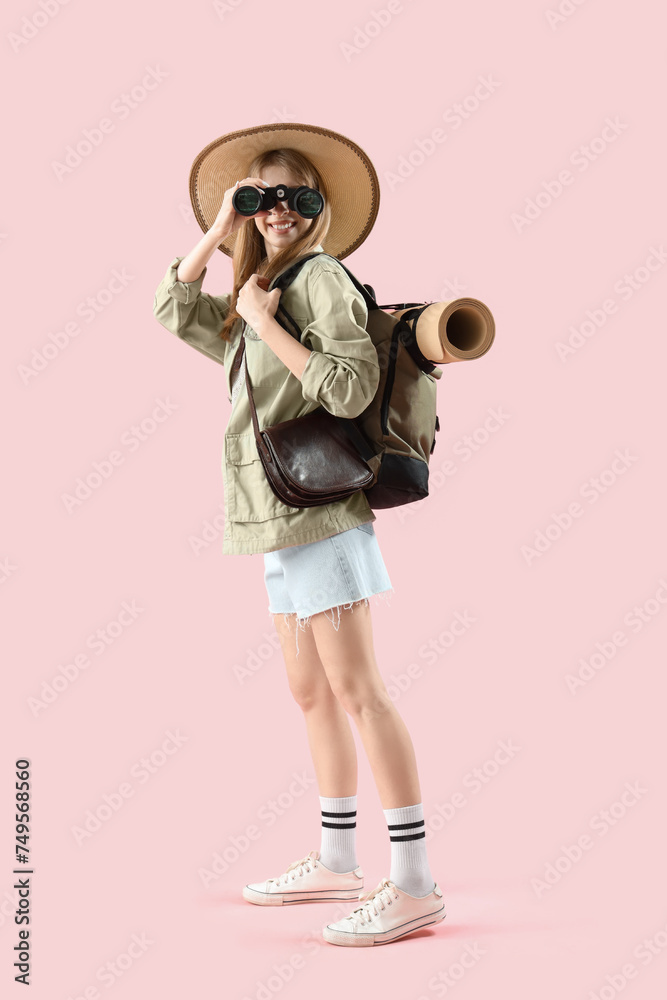 Female traveler with binoculars on pink background