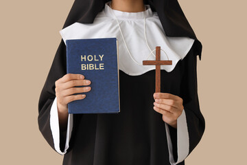 Young nun with Bible and cross on beige background