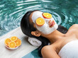 woman relax resting on a mat by the pool surrounded by water,with beauty facial mask and orange slices on her eyes and bowl of oranges at her side,health,lifestyle,skin care,wellness concept