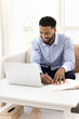 © fizkes - Cheerful young Black student guy watching online training lecture on laptop, writing notes, speaking on educational Internet conference meeting, using notebook. Vertical shot