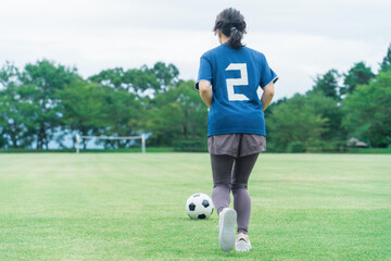 Poster - グランドでサッカーボールをドリブルするユニフォームを着た女性の後ろ姿
