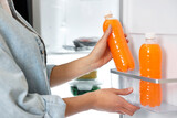 Fototapeta Kuchnia - Young woman taking bottle of juice out of refrigerator, closeup