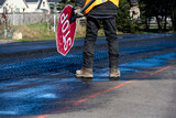 Fototapeta Desenie - Traffic control worker in orange reflective safety vest with temporary stop sign managing traffic in a road work construction zone
