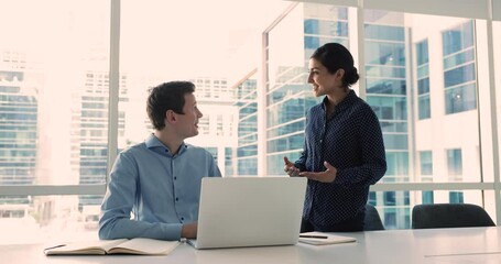 Canvas Print - Pretty Indian female mentor explaining task to young caucasian male colleague, working, talking met in city office, share opinion, provide project details, planning cooperation, take part in briefing