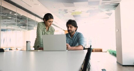 Canvas Print - In modern office, Indian colleagues collaborate, working use laptop. Serious workmates, mentor and apprentice discuss project details, share ideas, provide helpful information, learn new corporate app