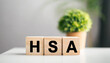 Wooden blocks spell 'HSA' on white table, symbolizing savings, healthcare, and investment in clean, minimalist setting