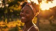 An African American woman, gazing off into a park at sunset, smiles.
