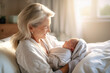 An elderly woman lovingly cradles a baby in her arms while sitting on a bed