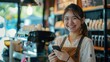 Asian barista woman standing success sme with cute smiling at city modern cafe and holding a smart phone in good day so happy. cheerful attractive girl waitress laughing and looking at cellphone.