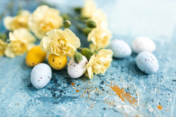 Canvas Print - Yellow beautiful flowers and blue and yellow colored easter eggs on a blue picturesque oil painting background close up. Mockups. Layout. Spring pastel background. Easter pastel contemporary backgroun