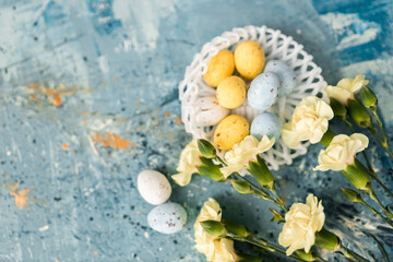 Wall Mural - Yellow beautiful flowers and blue, yellow colored easter eggs in wicker basket on a blue picturesque oil painting background close up. spring Mockups. Layout. Easter pastel contemporary background