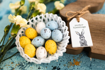 Canvas Print - Yellow beautiful flowers and blue, yellow colored easter eggs in wicker basket, and easter bunny on a blue picturesque oil painting background close up. spring Mockups.Layout. Easter pastel background