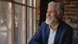 © Rando - Happy older businessman with a grey beard happily looking out the window.