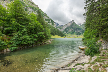 Beautiful summer view on lake Seealpsee in the Swiss alps, 2 rowing boats are lying in the water in the foreground. Cloudy sky. Wonderful hiking spot. Alpine lake with high mountains. Pine trees.