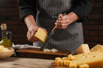 Wall Mural - Woman grating cheese at wooden table, closeup