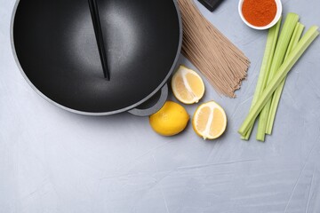 Wok, chopsticks and different products on grey table, flat lay. Space for text