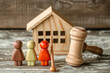 Wooden figurines of parents and children stand on table near toy house and judges hammer  