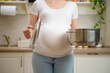 © Андрей Журавлев - A pregnant woman holds a lid from a saucepan in her hands, standing in a home kitchen. Pregnancy and proper nutrition while expecting a child