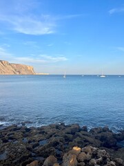 Wall Mural - White sail boats at the ocean, blue ocean horizon, rocky coast