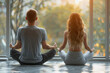 Yoga group concept. Young couple meditating together, sitting back to back on windows background.