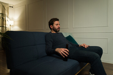 Wall Mural - Lonely man sitting on the couch alone drinking beer looking sad