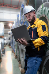 Wall Mural - Industrial engineer in safety helmet uniform jacket working in heavy steel engineering factory. Technician manager worker inspector using laptop in metalwork product manufacturing facility workplace