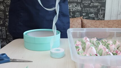 Wall Mural - A woman making packaging for homemade marshmallows. Trying on ribbon for tying the box of turquoise color. On the table zephyr tulips.