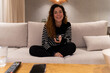 © Ruben - A woman is sitting on a couch with a remote in her hand. She is smiling and she is enjoying herself