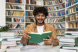 © Liubomir - A cheerful student deep in study amidst a pile of books in a university library setting, showcasing preparation for exams and academic dedication.