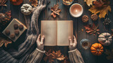 Fototapeta  - A person is holding a book open on a table with a pumpkin, a candle, and a bowl of cookies. The scene is cozy and inviting, with the book and the pumpkin creating a warm atmosphere