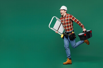 Wall Mural - Full body side view young employee laborer man in red shirt hardhat hat work hold toolbox isolated on plain green background Instruments accessories for renovation apartment room Repair home concept