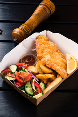 Wall Mural - Fried breaded chicken fillet with lemon, rustic potato wedges, vegetable salad and sauces in a paper box.