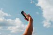 © Centric  - A man's arm extends upwards, holding a smartphone against a backdrop of fluffy clouds and blue sky