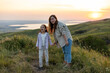 © Irina Mikhailichenko - Young mother with her baby surprised girl daughter at sunset on the background of the lake. Family holiday on pond. Portrait mom with child together in nature. Happy Mothers Day.