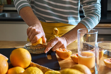 Female hands making homemade grapefruit juice with hand citrus juicer. Anonymous woman preparing fresh grapefruit juice in the kitchen.